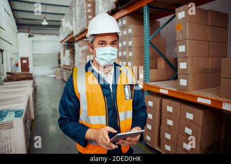 Portrait of a male supervisor in hardhat and protective vest holding digital tablet in warehouse Stock Photo
