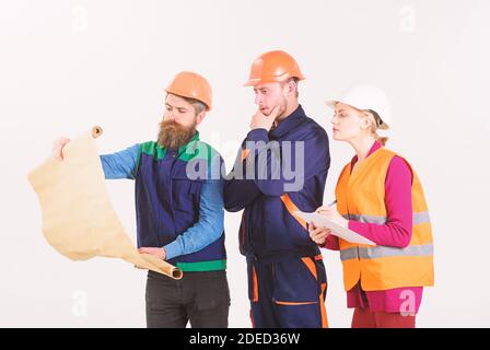 Men and woman in helmets, architects on thoughtful faces looks at drawing, plan, blueprint, project, white background. Engineering concept. Team of builder, engineer, architect work on project. Stock Photo