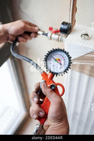 Closeup plumber filling pipes with pressurized air to inspect for leaks in new heating system installation. Worker using manometer, checking gas tightness of heating system. Concept of home renovation Stock Photo