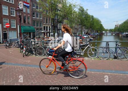 AMSTERDAM, NETHERLANDS - JULY 10, 2017: Cyclist crosses Herengracht canal in Amsterdam, Netherlands. Amsterdam is the capital city of The Netherlands. Stock Photo