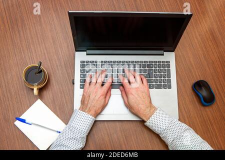 man hands typing on computer seen from above, at home or office table with coffee and note book Stock Photo