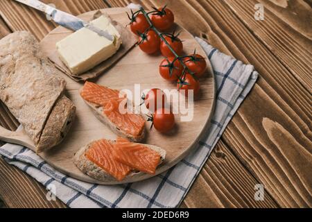 Two sandwiches with smoked salmon and other food on old board on rustic wooden background. Top view Stock Photo
