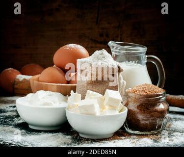 Baking ingredients: milk, butter, flour, sugar, eggs and rolling pin on a floured table in a rustic style, selective focus Stock Photo