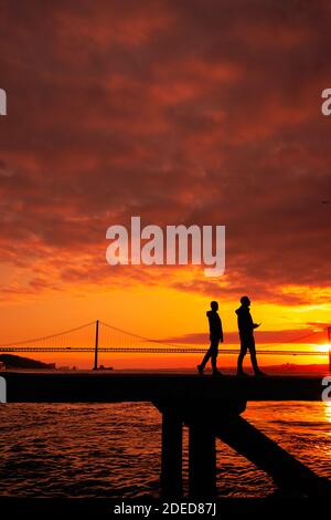 Silhouette of lovers walking with a  bridge in the background sunset time Lisbon Stock Photo