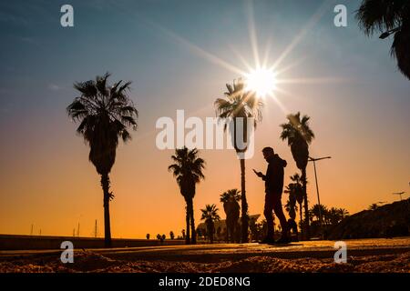 Silhouette of young man with mobile phone walking at sunset Stock Photo