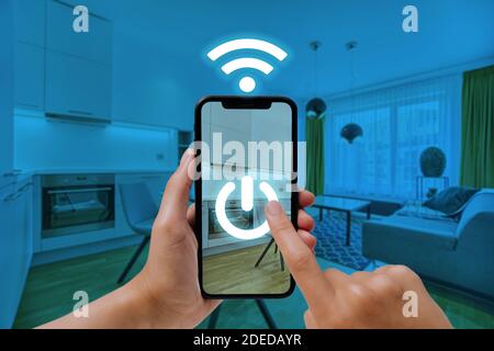 Concept on home automation. A woman uses a smartphone to control electronic devices and appliances in the house. Internet of Things, IoT. Stock Photo