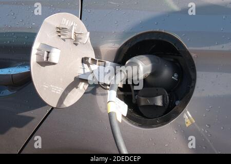 A hybrid car uses an EV (electric vehicle) charger in a supermarket car park. Stock Photo