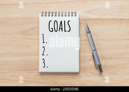 Top view of notepad with Goals List on wooden table, goals concept. Stock Photo