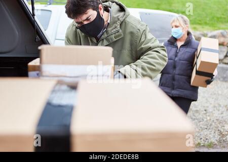 Parcel service subcontractor stacks parcels in car at Christmas with face mask because of Covid-19 Stock Photo