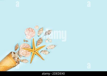 A wafer cone with sea shells and a yellow starfish on a light blue background with copy space Stock Photo