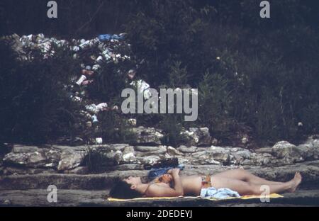 1970s Photos (1973) -  Sublime indifference? tourist sunbathes on Lake Ozark shore within yards of unsightly rubbish heap  (Lake of the Ozarks Missouri area) Stock Photo