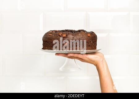 Woman holding a cake plate with a chocolate cake in front of wall with subway tiles Stock Photo