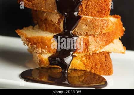 Chocolate sauce on vanilla cake slices on a white plate in a close up view Stock Photo