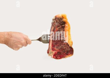 Man holding a big fork with a matured steak isolated on a white background Stock Photo