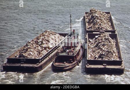 1970s Photo - (1973) -  Tugboat herds garbage scows down the East River from a transfer point in Manhattan Stock Photo