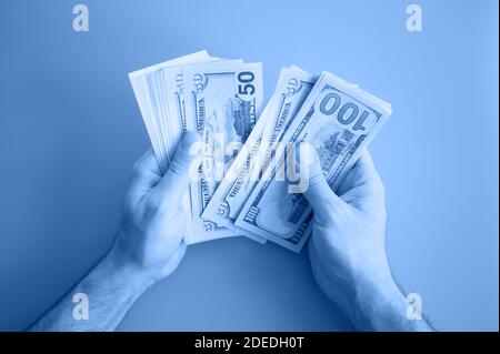 men's hands hold and count 100 and 50 dollar bills. toned in classic blue color trend 2020 year Stock Photo