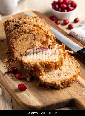 Cranberry orange sweet bread sliced on wooden cutting board with bowl of cranberries in background Stock Photo