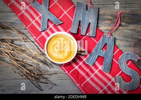 Cup of creamy coffee and wooden letters XMAS on a red kitchen towel. View from above. Stock Photo