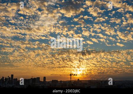 Cranes in the foreground and colorful altocumulus clouds sky in background in sunset time. City landscape at dusk. A concept of economic development. Stock Photo