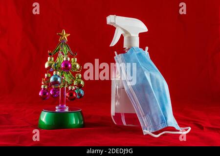 Mini Christmas tree next to an antiseptic spray wearing a blue facemask. Christmas in the covod-19 era concept photo. Stock Photo