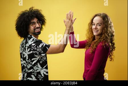 Mature man and young woman in a studio on yellow background, giving high five. Stock Photo