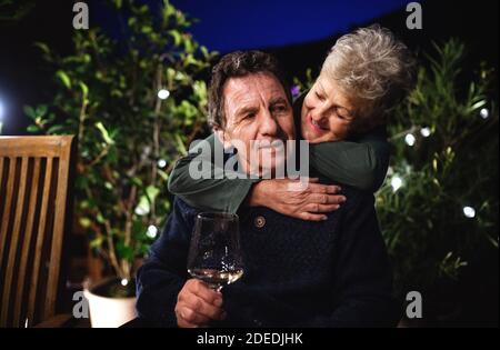 Senior couple with wine in the evening on terrace, hugging. Stock Photo