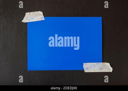 Rectangular sheet of blue paper glued with adhesive tape to a black background. Minimalistic multitask background. Stock Photo