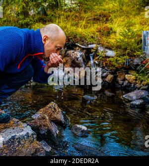 Hiker drinking clean glacial water from a small stream. Close up. Stock Photo
