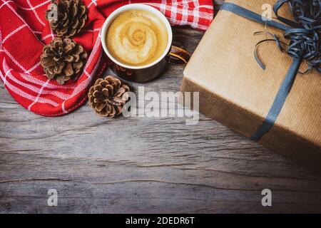 Christmas background with gift box, cup of coffee, red kitchen towel and pine cones on rustic wooden table. Stock Photo