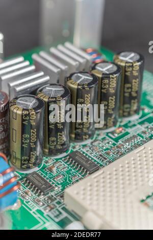 Close up detail of a row of 5 electrical aluminium electrolytic capacitors on a green printed computer motherboard (pcb). Aluminium cooling fins. Stock Photo