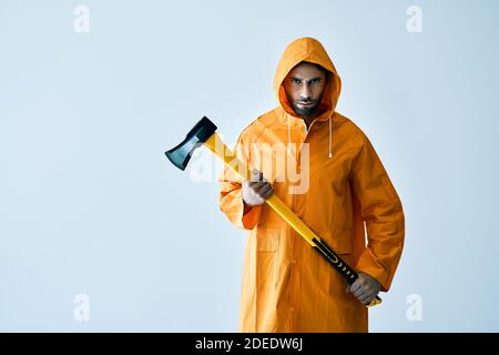 Young serious man in bright raincoat holding big axe in hands with copy space. Brutal male, lumberjack, fisherman with ax Stock Photo
