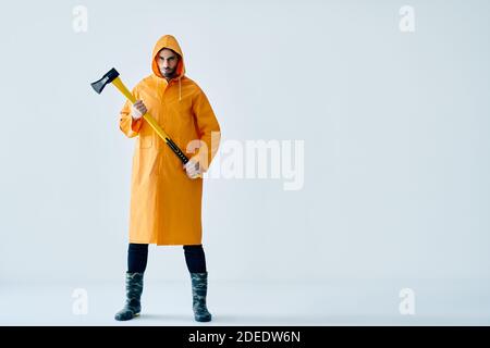 Full length portrait of young handsome man in bright raincoat holding big axe with copy space. Brutal male, lumberjack, fisherman with ax Stock Photo
