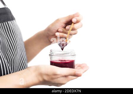 Woman hand holding a spoon with berry jam in jar in clipping path. Stock Photo