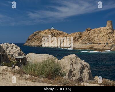 Pietra lighthouse on top of the stiff rocky cape in Northern Corsica under a bright blue sky Stock Photo