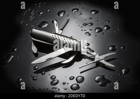 A high angle shot of metal multi-purpose knife with water droplets isolated on black background Stock Photo