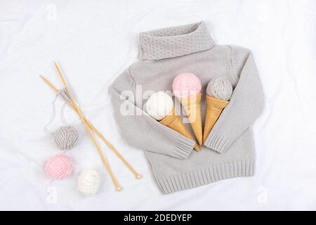 Three ice cream from yarn and waffle cones on a gray knitted sweater, wooden knitting needles on white background. Knitting, hobby and handmade concep Stock Photo
