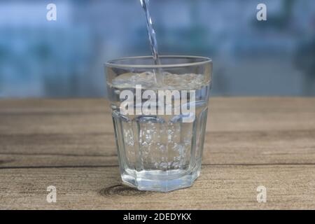 Fresh water pouring into glass on wooden table.Blurred background Stock Photo