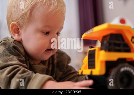 Little boy with blond hair plays with yellow truck on the floor. high quality Stock Photo