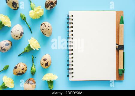Spring yellow flowers, organic natural quail eggs and open craft notebook with pen on blue background. Happy Easter and zero waste concept. Mock up Cr Stock Photo