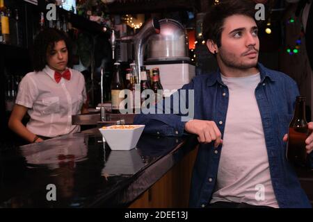 Young caucasian man with a beer bottle in his hand watching TV, football match in a bar. Waitress on the background. Stock Photo