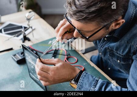 High angle view of repairman with screwdriver fixing smashed display of tablet at workplace on blurred background Stock Photo
