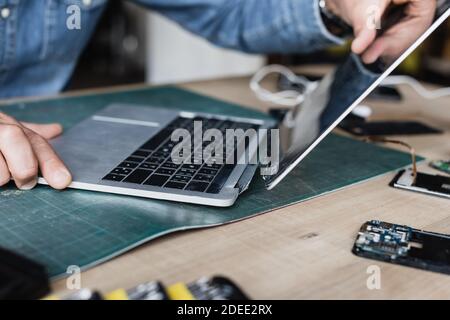 Cropped view of repairman holding damaged laptop at workplace on blurred background Stock Photo