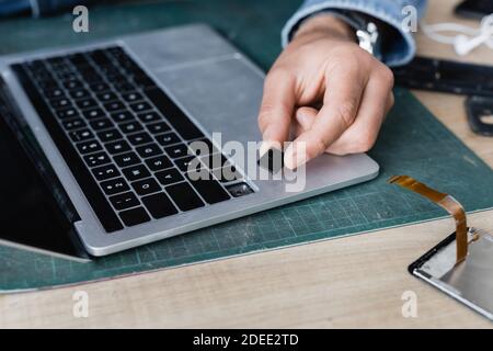 Cropped view of repairman holding broken key of laptop keyboard at workplace on blurred background Stock Photo