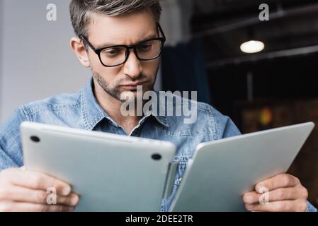 Focused repairman in eyeglasses looking at damaged laptop on blurred foreground Stock Photo
