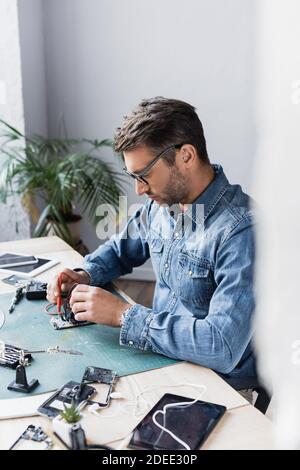 Repairman holding sensors of multimeter of disassembled part of mobile phone on table on blurred foreground Stock Photo