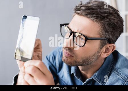 Focused repairman in eyeglasses looking at broken touchscreen in office Stock Photo