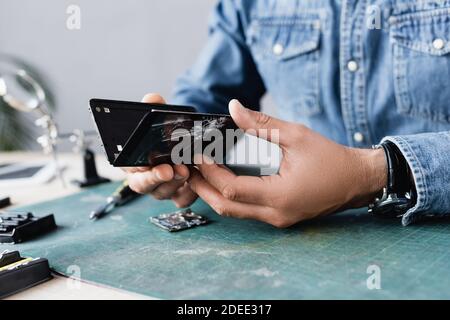 Close up view of disassembled parts of broken smartphone in hands of repairman at workplace on blurred background Stock Photo