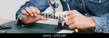 Cropped view of repairman holding disassembled part of mobile phone near magnifier at workplace, banner Stock Photo