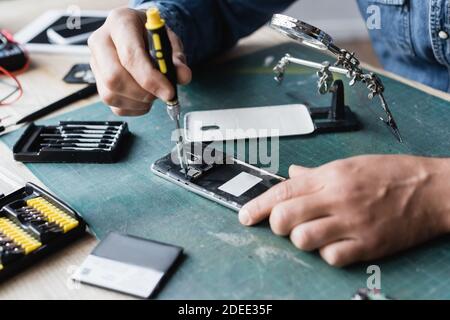 Cropped view of repairman with screwdriver fixing disassembled mobile phone at workplace on blurred background Stock Photo