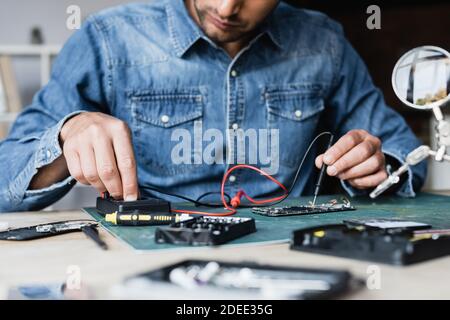 Cropped view of repairman using multimeter while holding sensor on disassembled part of mobile phone on blurred foreground Stock Photo